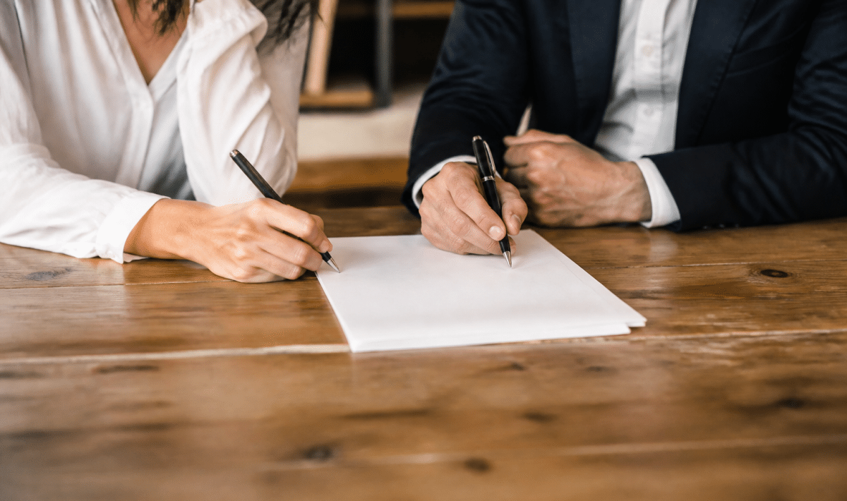 Deux personnes signant document papier sur table bois