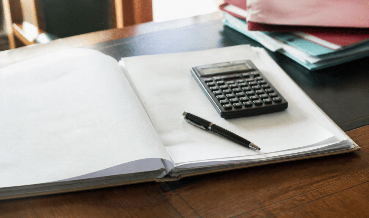 Document notarial ouvert sur bureau avec calculatrice et stylo poses dessus