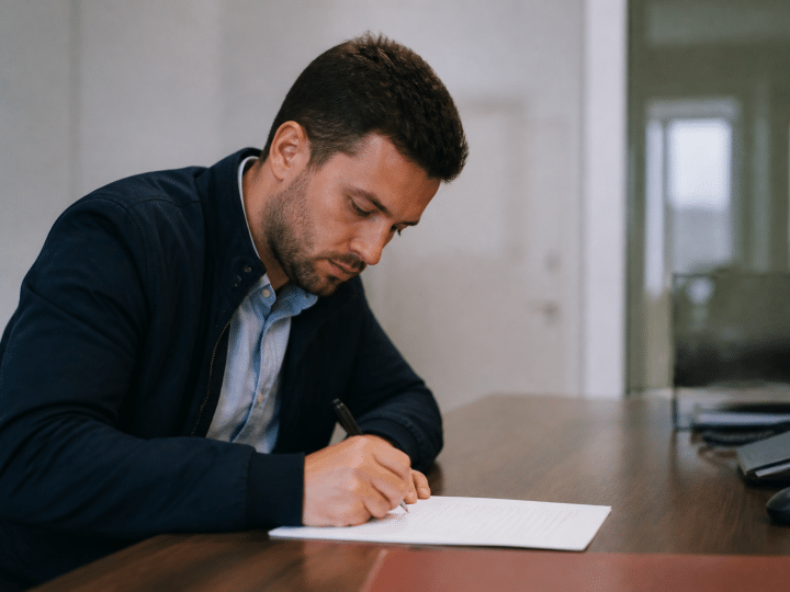 Homme assis face a un bureau signant un document officiel
