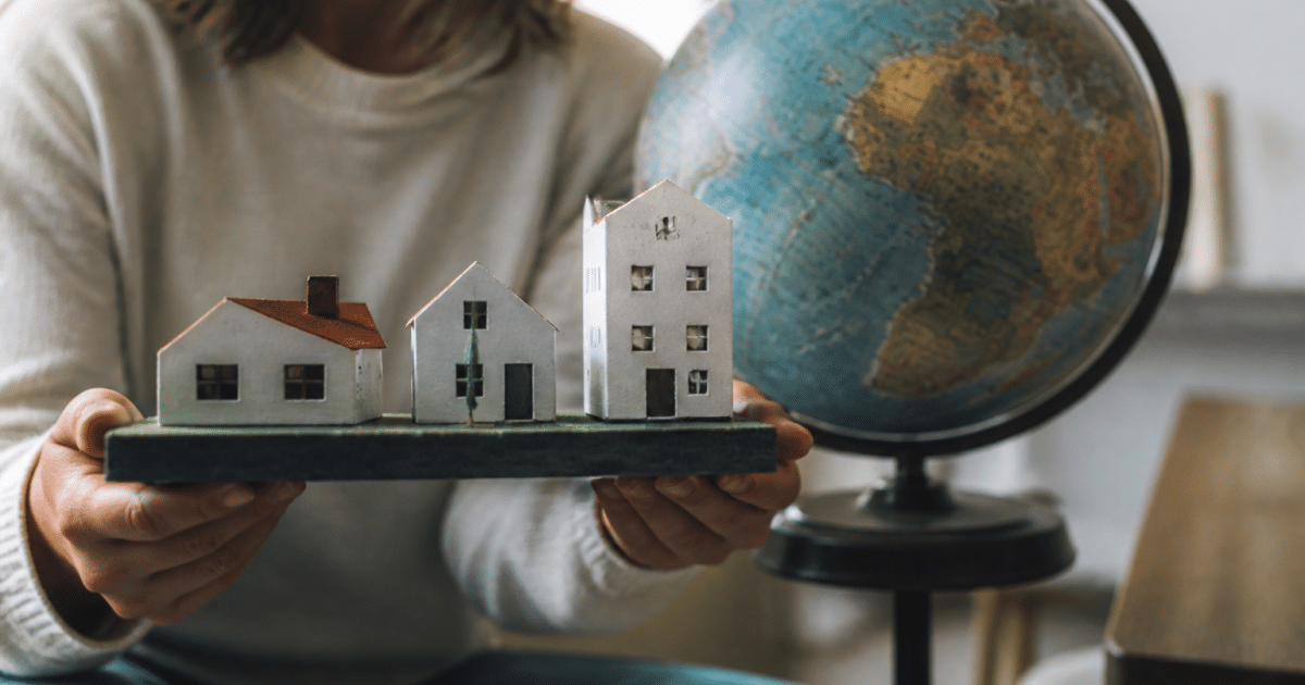 Mains tenant maquette maisons devant globe terrestre rotatif
