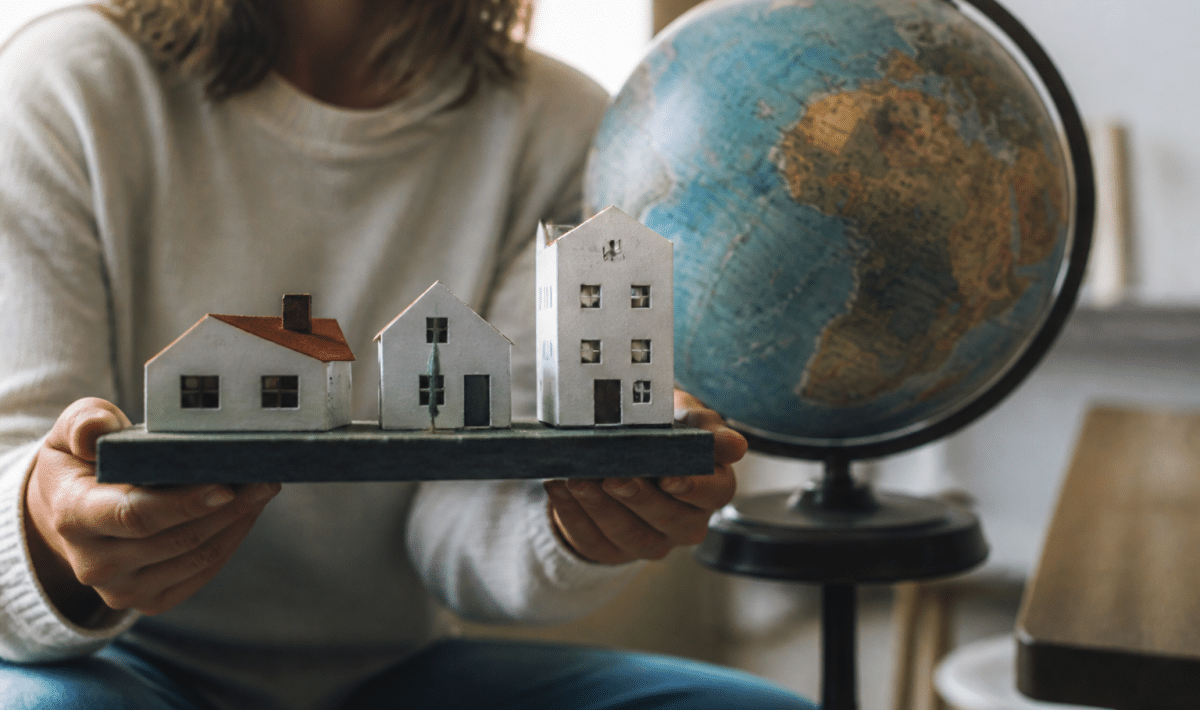 Mains tenant maquette maisons devant globe terrestre rotatif