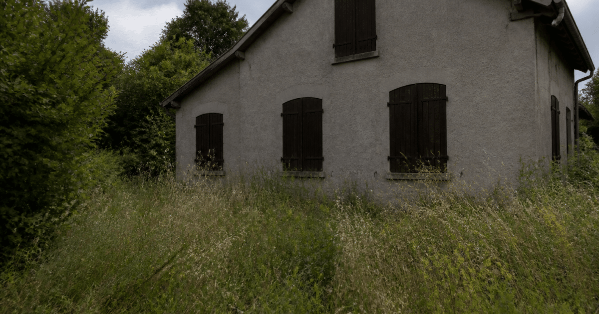Maison vide abandonnée avec volets fermes et herbes hautes