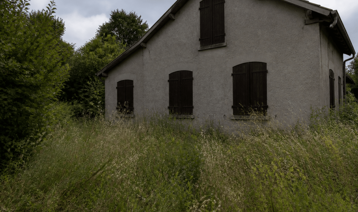 Maison vide abandonnée avec volets fermes et herbes hautes