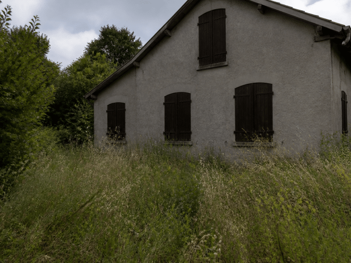 Maison vide abandonnée avec volets fermes et herbes hautes