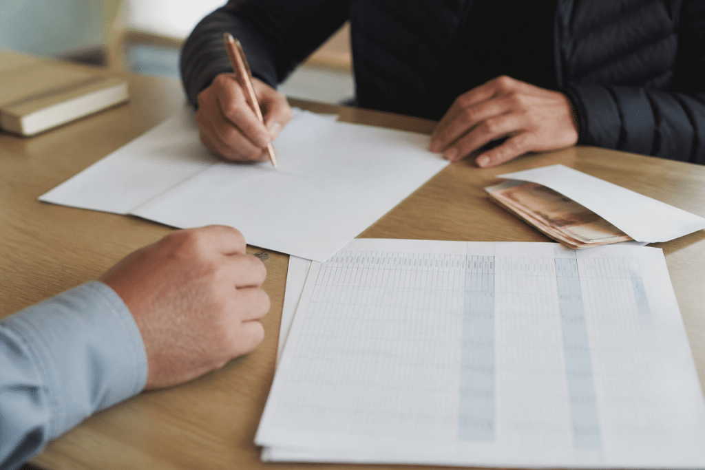 Mains signant contrat avec relevé bancaire et enveloppe argent